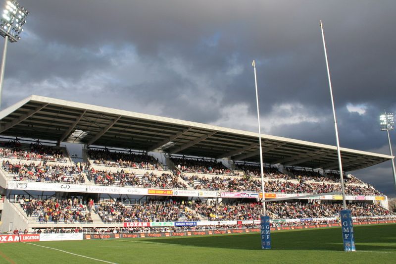 La tribune Auvergne du stade Marcel-Michelin à Clermont-Ferrand, remplie de supporters, avec les poteaux de rugby et les projecteurs