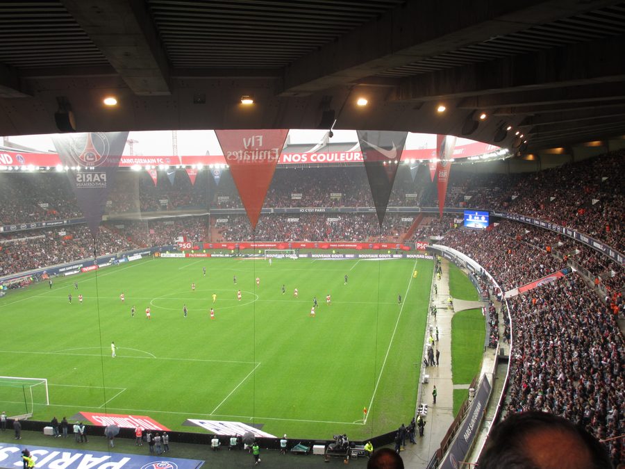 Le Parc des Princes plein en tribunes lors d'un match du PSG, avec les bâches Paris Saint-Germain et le terrain en contrebas