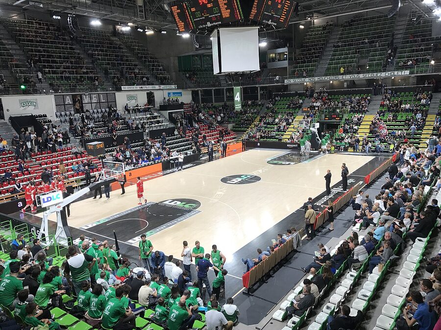 Vue de la salle de l'Astroballe depuis les gradins, avec le parquet, les tribunes vertes et les joueurs à l'échauffement avant un match de Pro A de basket