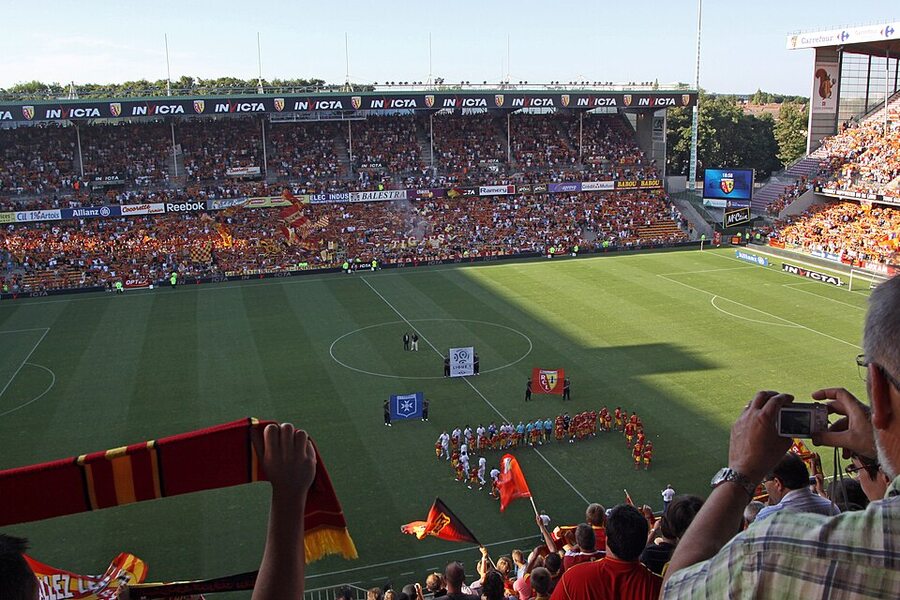 Les supporters du RC Lens dans les tribunes du stade Bollaert-Delelis, avec écharpes et drapeaux, pendant l'entrée des joueurs sur la pelouse