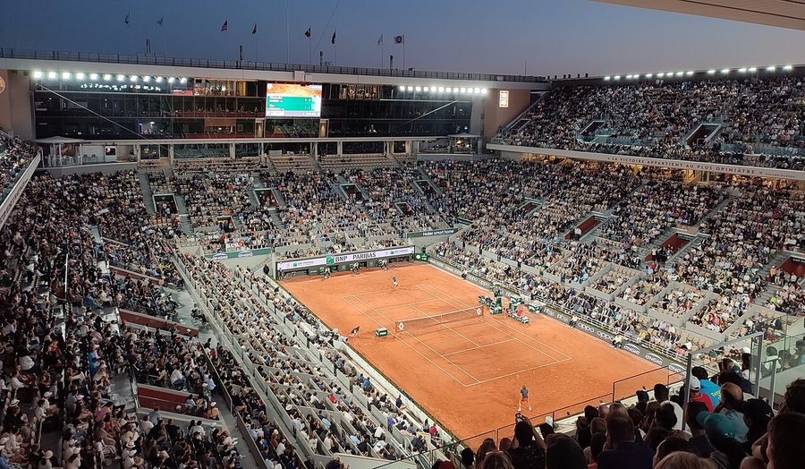 Le court Philippe-Chatrier de Roland-Garros rempli de spectateurs lors d'un match en soirée, vu depuis les tribunes hautes