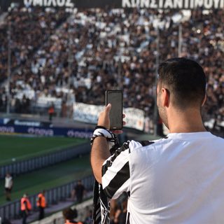 Supporter filmant avec son smartphone depuis une tribune pleine avant un match de football