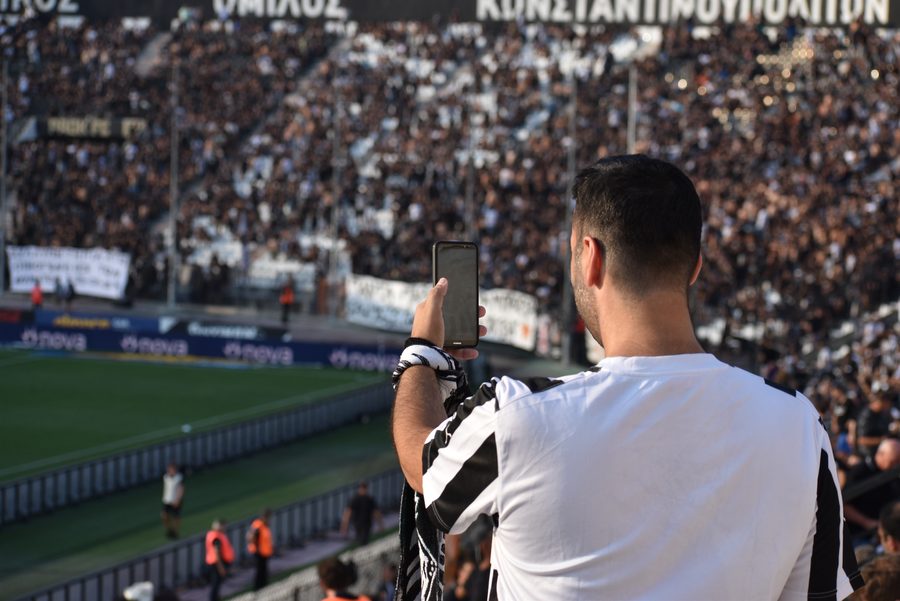 Supporter filmant avec son smartphone depuis une tribune pleine, avant un match de football