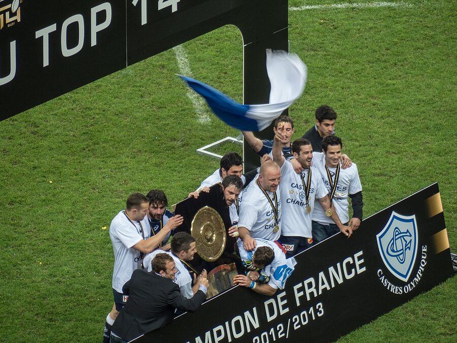 Les joueurs du Castres Olympique rassemblés autour du Bouclier de Brennus sur la pelouse du Stade de France, devant un panneau Champion de France 2012-2013
