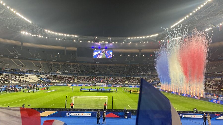 Supporters agitant des drapeaux tricolores devant des fumigènes bleu-blanc-rouge avant un match de l'équipe de France au Stade de France