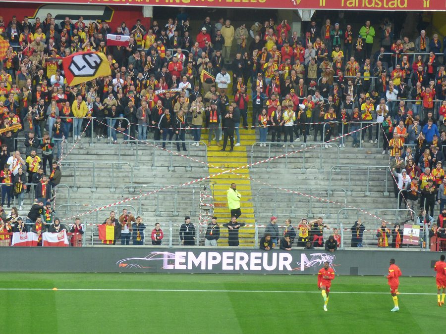 Tribune garnie de supporters lensois et pelouse éclairée lors d'un match de Ligue 1